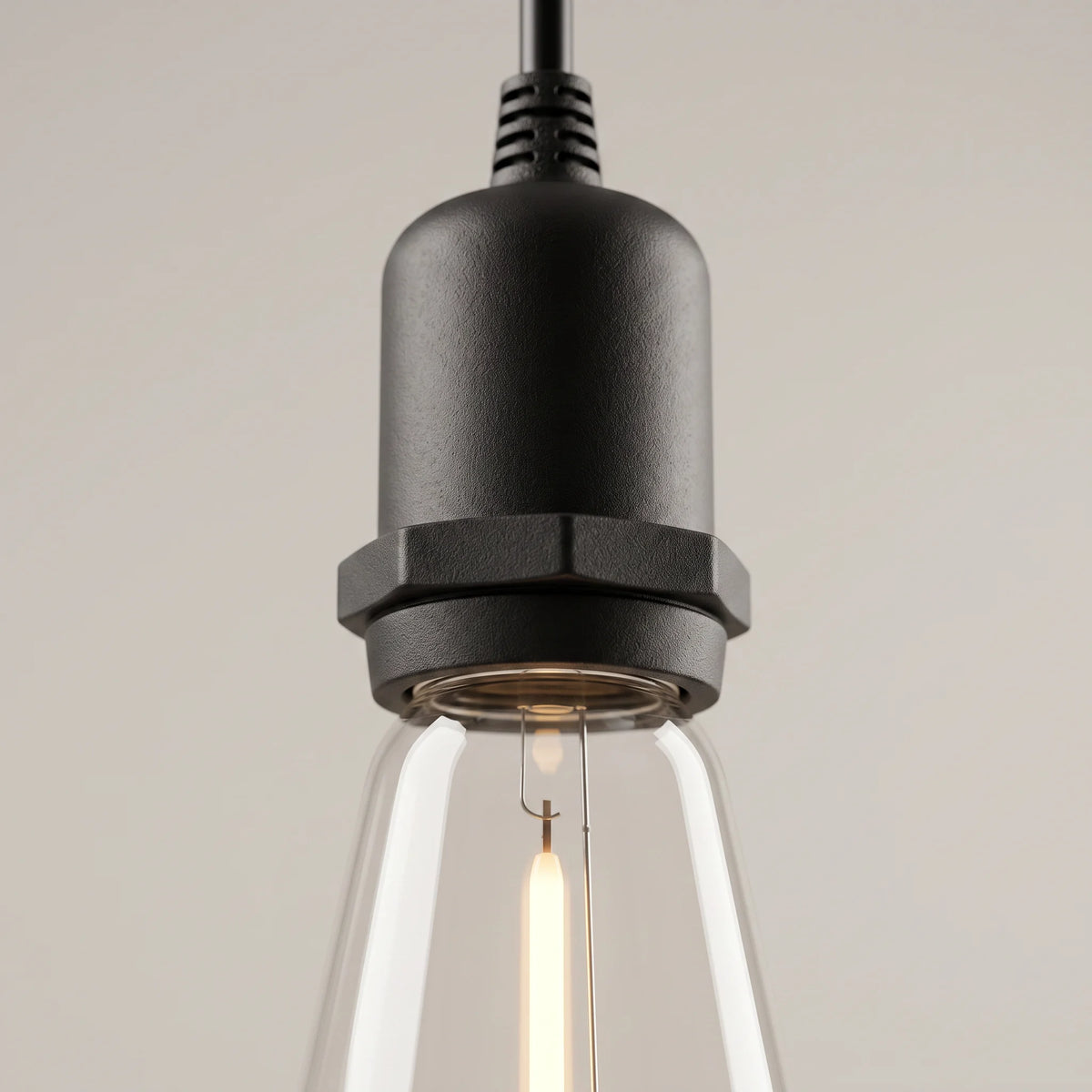 Close-up of one black lamp socket with its ribbed cable grip and the lit filament bulb below