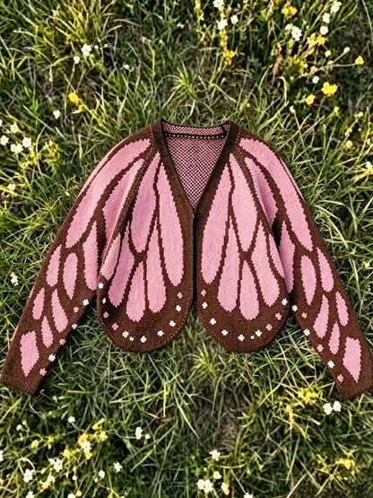Butterfly wing knit cardigan in soft pink with brown edging, laid flat on grass