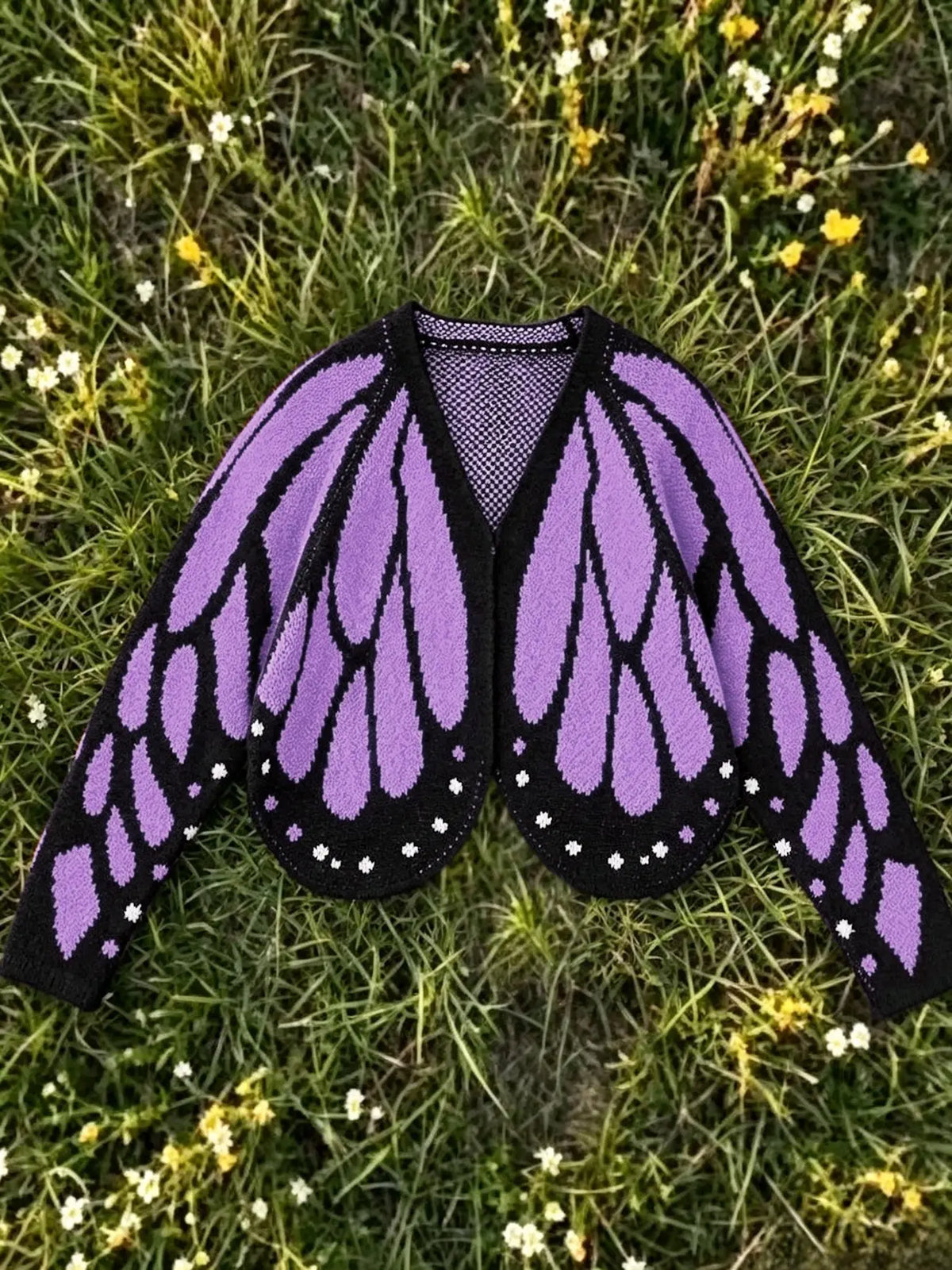 Butterfly wing knit cardigan in purple and black, laid flat on grass