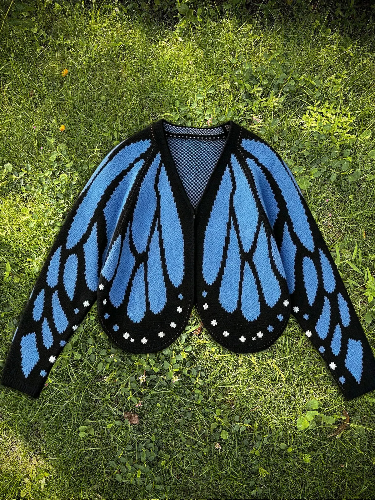 Butterfly wing knit cardigan in denim blue and black, laid flat on grass