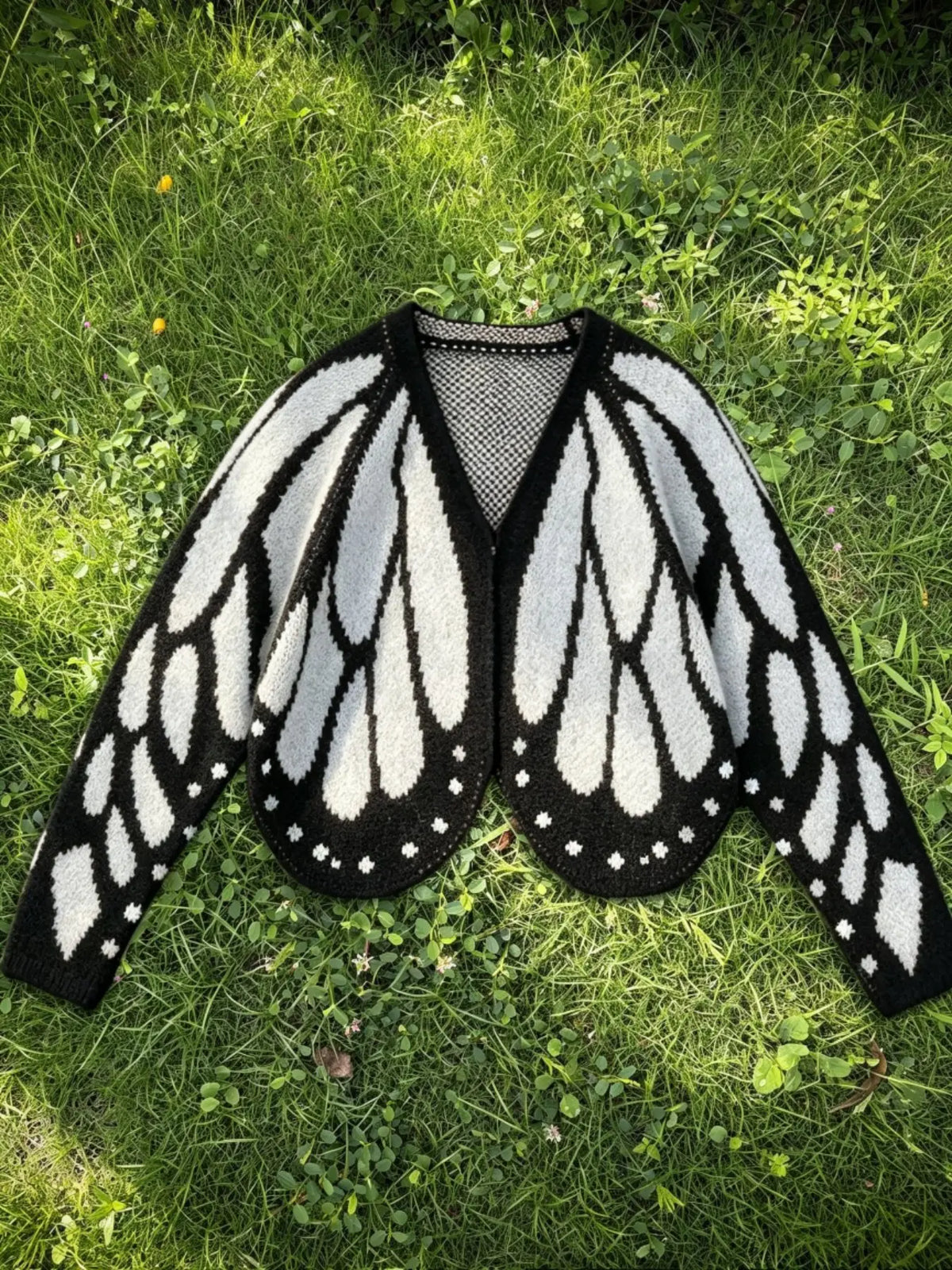 Butterfly wing knit cardigan in white and black, laid flat on grass