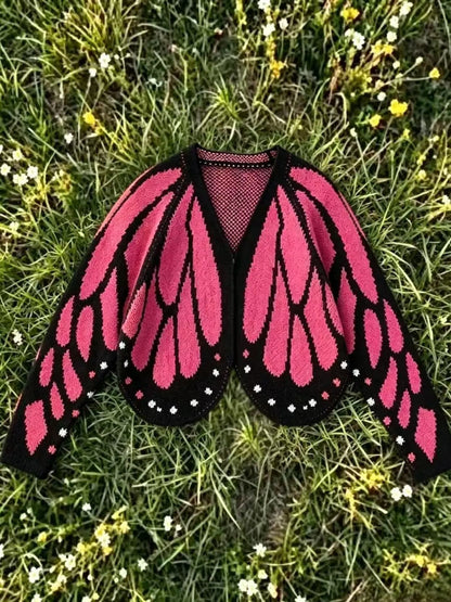 Butterfly wing knit cardigan in deep rose pink and black, laid flat on grass