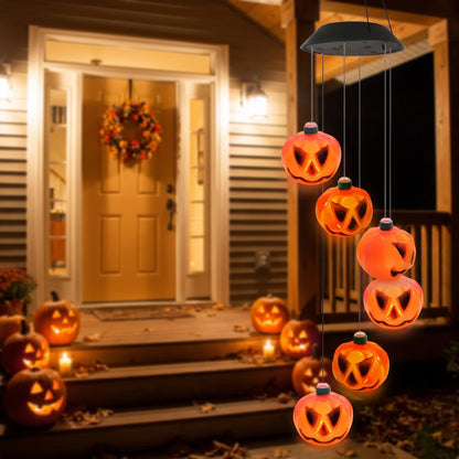Solar pumpkin wind chime glowing orange on a front porch at dusk beside carved jack-o'-lanterns and an autumn wreath