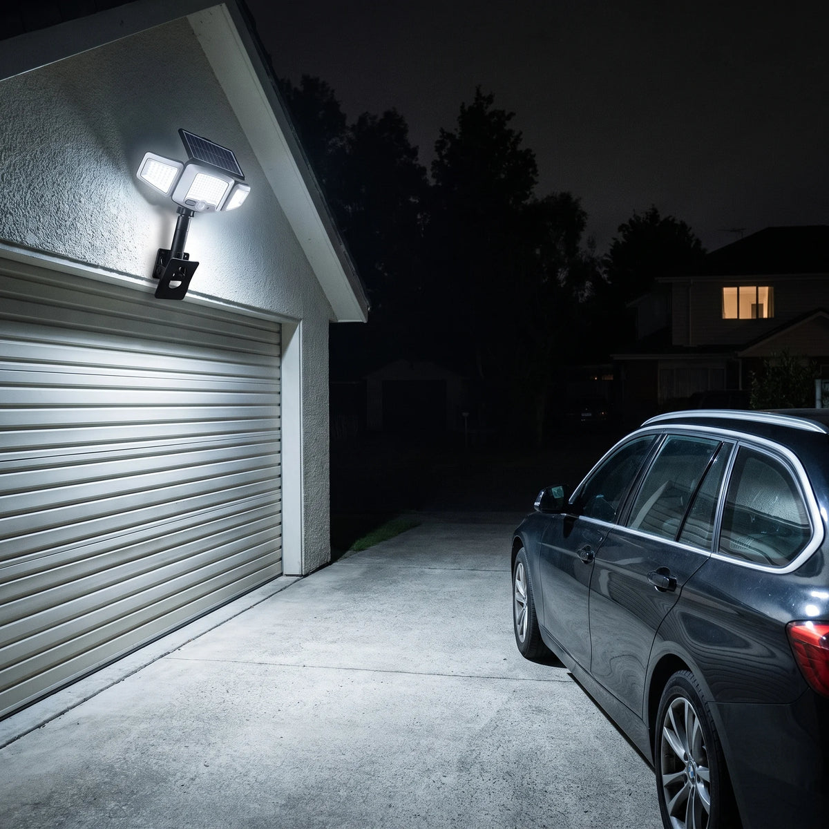 Solar flood light on a garage wall lighting the driveway and a parked car at night