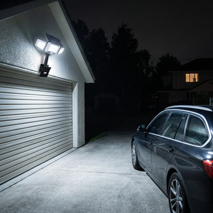 Solar flood light on a garage wall lighting the driveway and a parked car at night