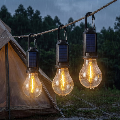 Three solar camping bulb lights clipped to a guy-line in evening rain, water beading on the glass