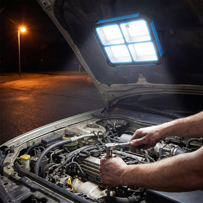 Work light stuck by its magnetic back under a raised car hood, lighting a mechanic's hands