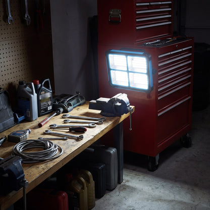 Work light clinging magnetically to a red rolling tool chest, lighting a garage workbench