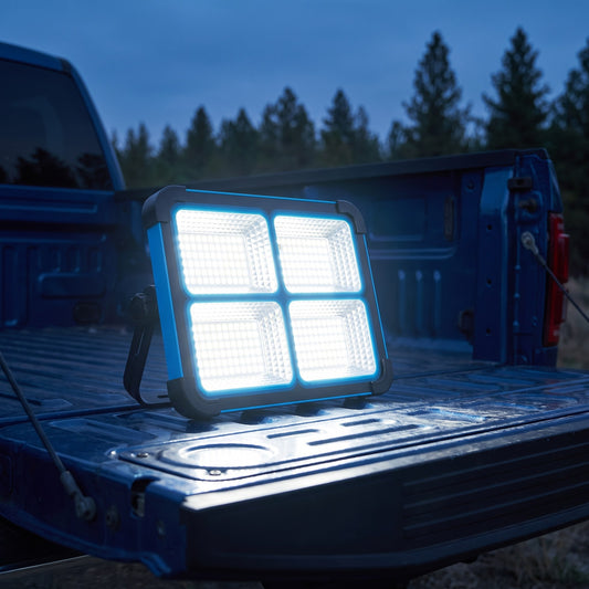 Blue solar LED work light standing on a pickup tailgate at dusk, all four panels lit