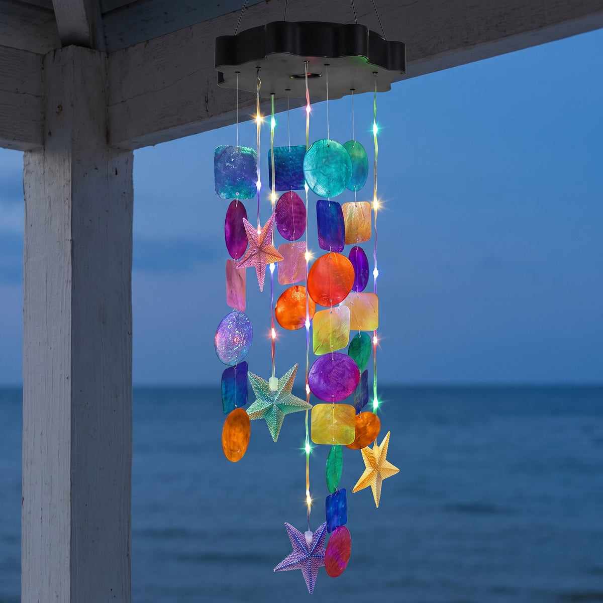Solar seashell chime lit at dusk above the sea