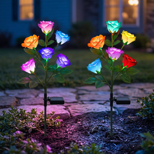 Solar glow rose stake lights glowing in a garden bed at dusk