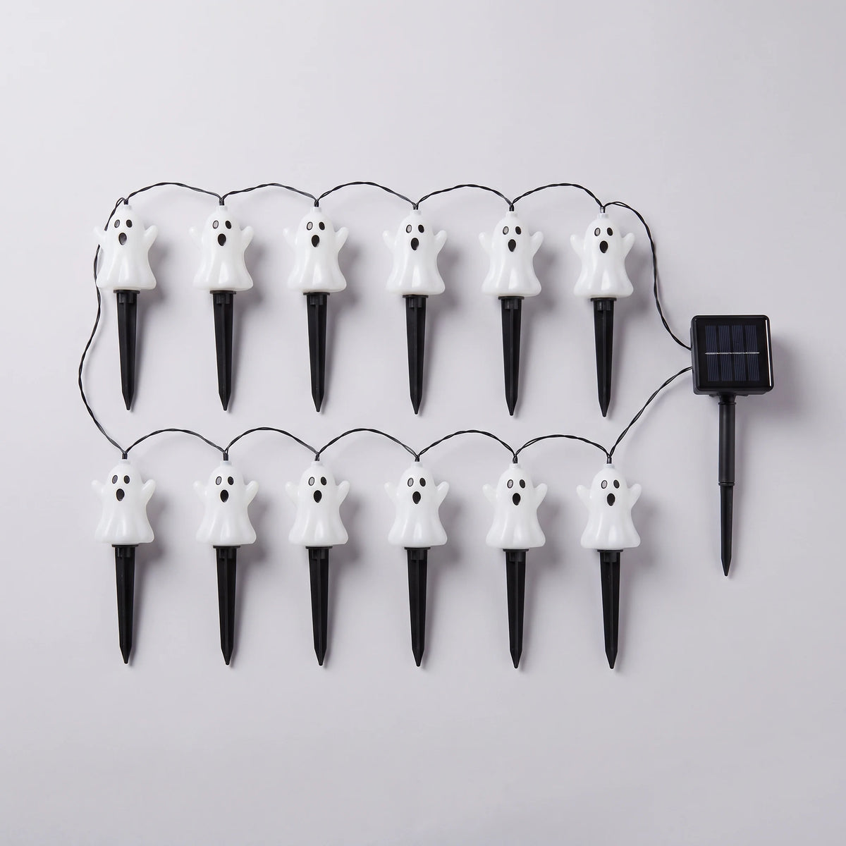 Twelve white ghost stake lights wired to a single solar panel, laid out flat on a pale grey background