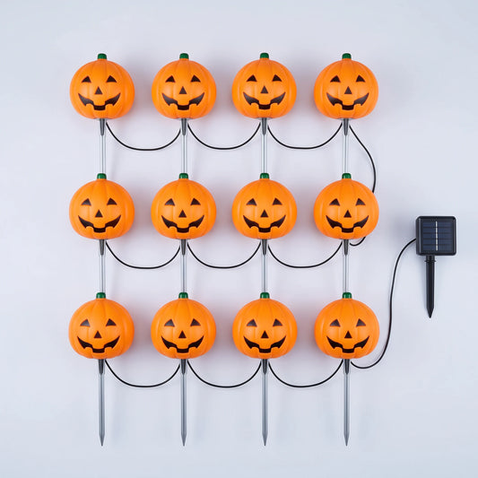 Twelve orange jack-o-lantern stake lights wired to a single solar panel, laid out flat on a pale background