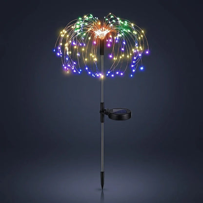 Single solar firework stake light lit against a dark background, copper wire sprays of multicoloured LEDs above a slim pole with a round solar panel