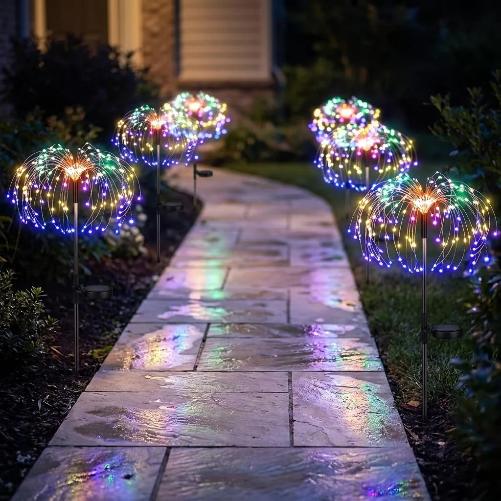 Five firework stake lights lining a damp stone path at night, colours reflecting on the paving