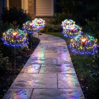 Five firework stake lights lining a damp stone path at night, colours reflecting on the paving