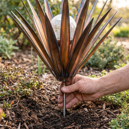 Hand pushing the ground stake of a metal agave solar light into garden soil, showing its size