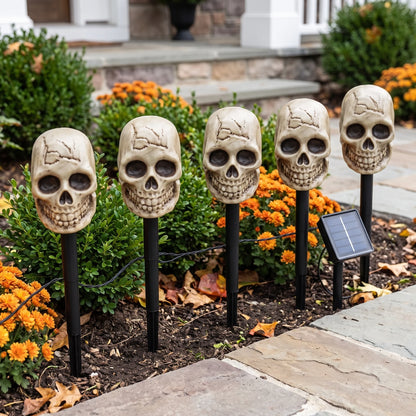 The same five skull stakes unlit in daylight, bone-coloured heads on black spikes with the solar panel at the end of the run