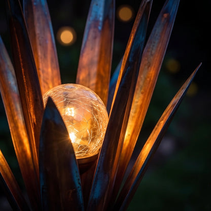 Close-up at night of the frosted crackle-glass solar orb glowing between copper agave blades