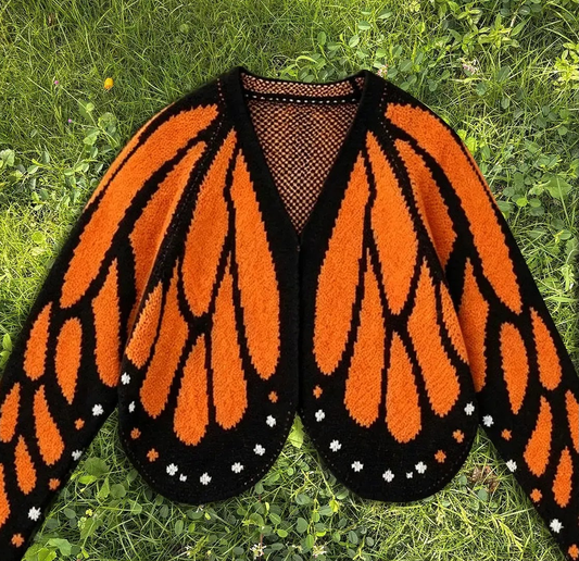Butterfly wing knit cardigan in orange and black monarch pattern, laid flat on grass