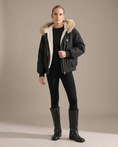A woman wearing the black bomber jacket open over black leggings and knee-high boots