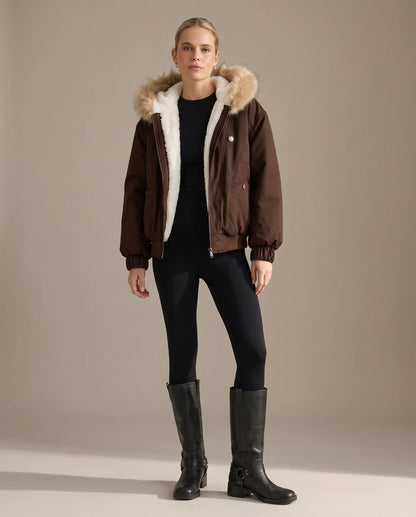 A woman wearing the mocha brown bomber jacket open over black leggings and knee-high boots