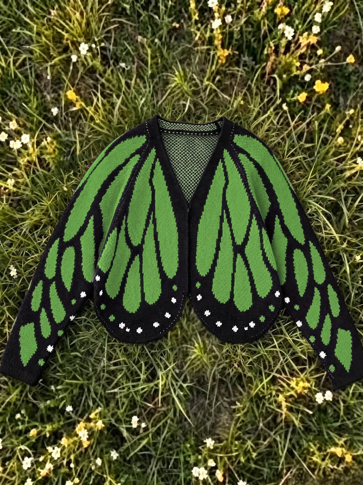 Butterfly wing knit cardigan in grass green and black, laid flat on grass